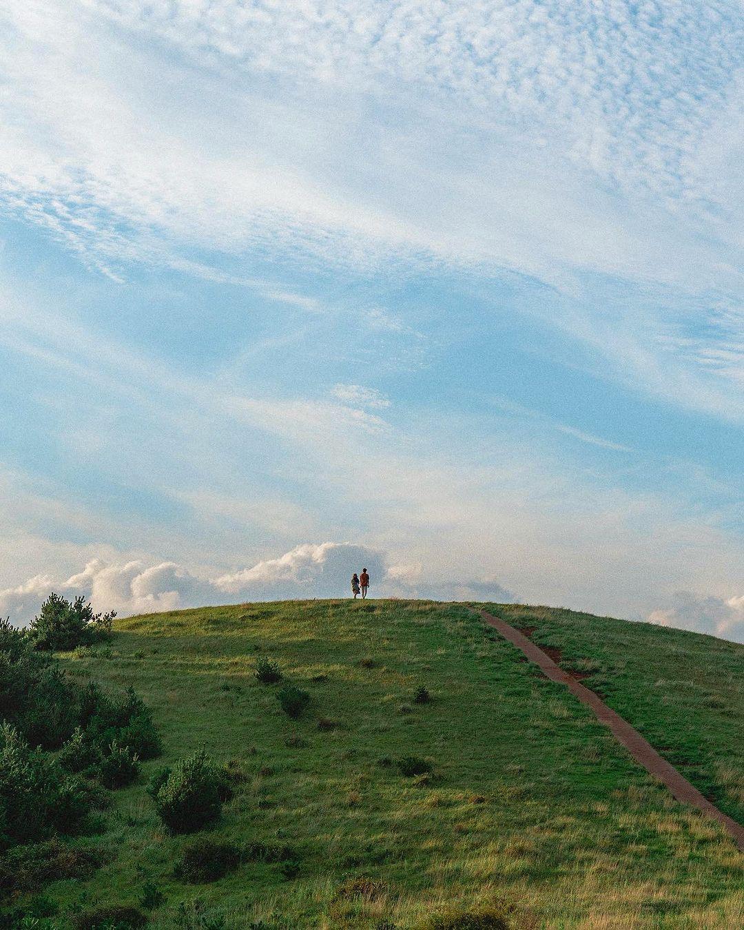 Zwei Personen auf einem grasbewachsenen Hügel unter einem bewölkten Himmel