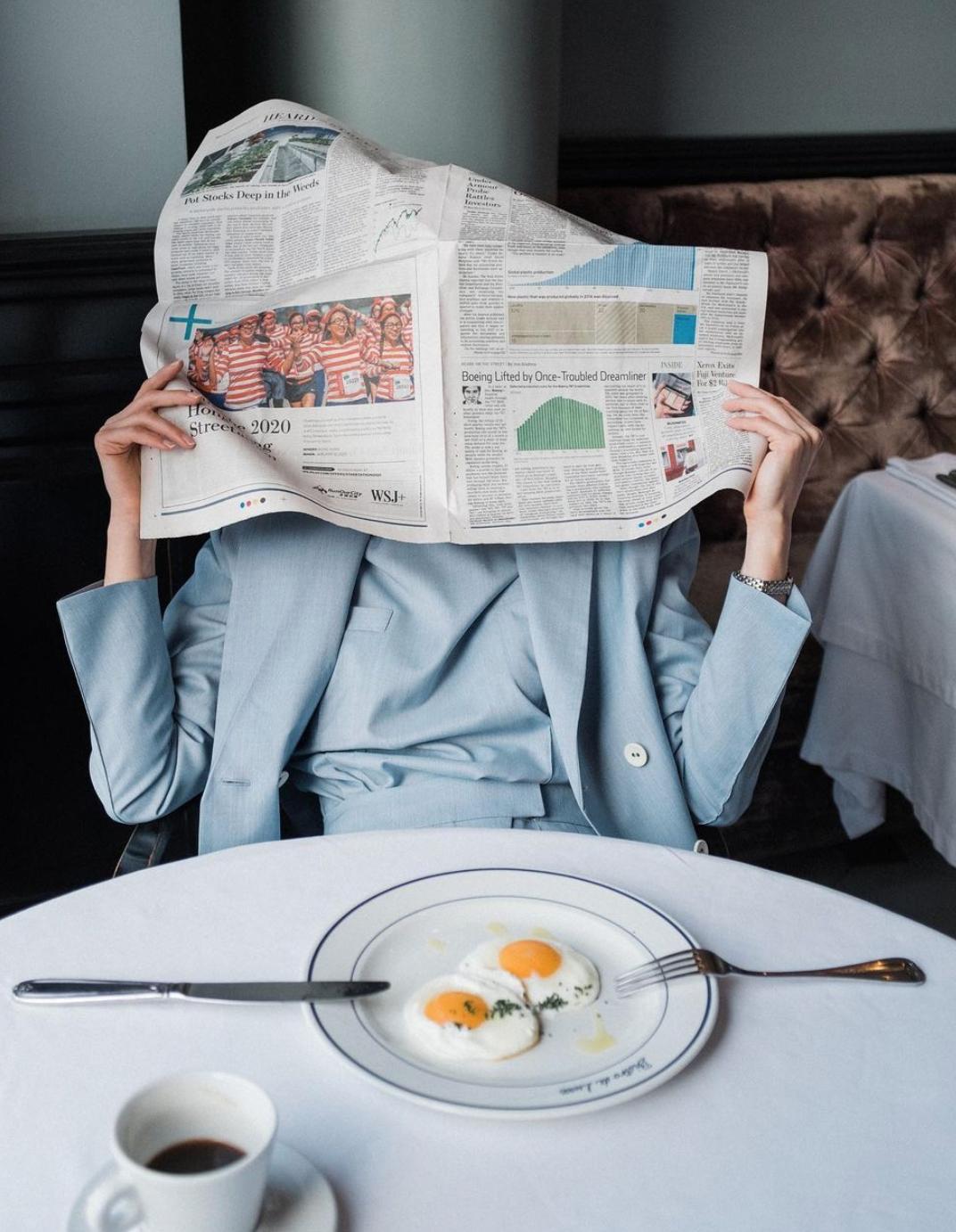 Frau im blauen Anzug liest Zeitung beim Frühstück und reflektiert über die Relevanz von Zeitungen in der heutigen Zeit.